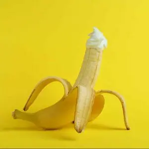 Banana with whipped cream on yellow background